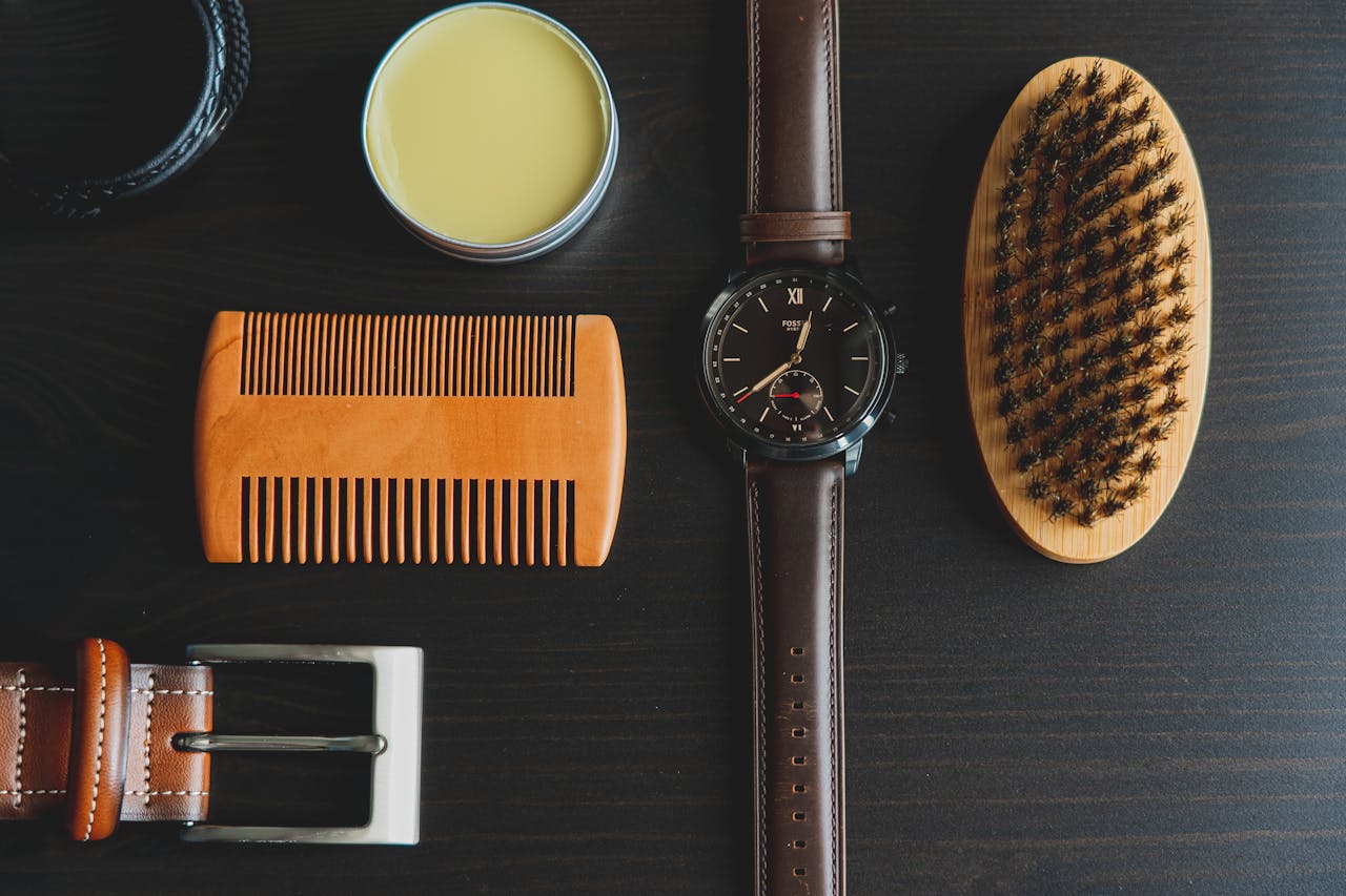 Flat lay of men's grooming accessories including watch, brush, comb, and pomade.